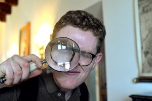 young man holding a magnifying glass in front of one eye